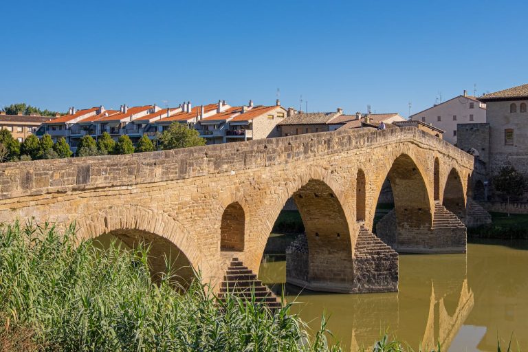 Puente la Reina stone bridge arching over a calm river on a sunny day in Navarra, Spain.